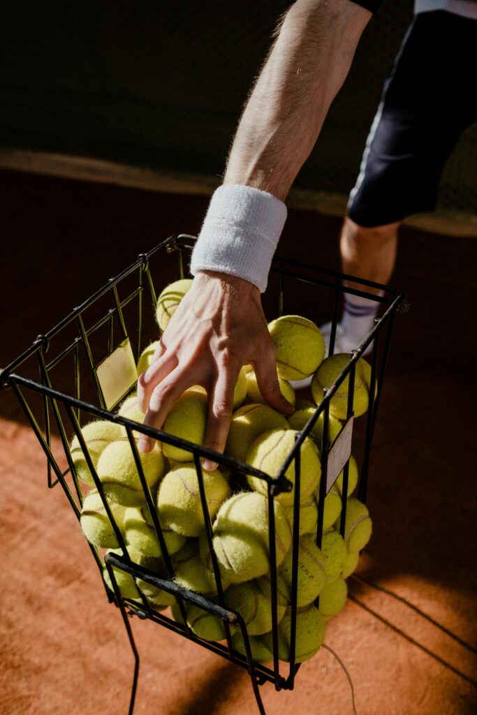 A tennis player collecting balls from a basket on a clay court, highlighting a close-up shot and sportive theme.
